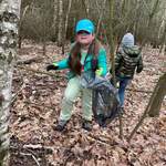 dziewczynka w czapce z daszkiem trzyma worek i sprząta śmieci w lesie.jpeg