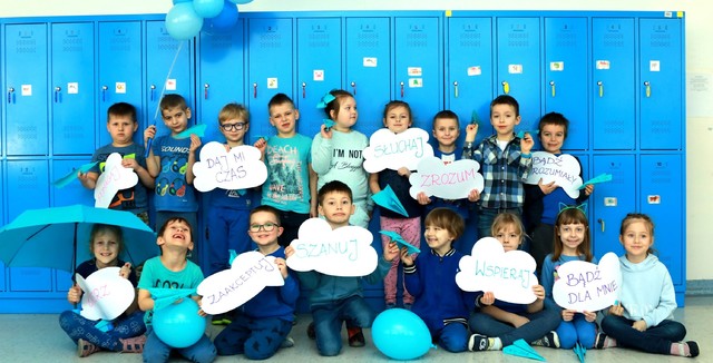 Na zdjęciu znajduję się grupa siedemnaściorga  dzieci 7-letnich, pozujących na tle niebieskich szafek szkolnych.jpg