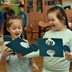 Zdjęcie prezentuje dwie wesołe dziewczynki próbujące połączyć w powietrzu dwa duże niebieskie puzzle.jpg