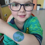 uśmiechnięty chłopiec prezentuje namalowaną kulę ziemską na ręce.jpg