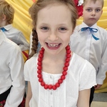 roześmiana dziewczynka w białej bluzce, czerwonych koralach i wianku, z tyłu chłopiec w białej koszuli.jpg